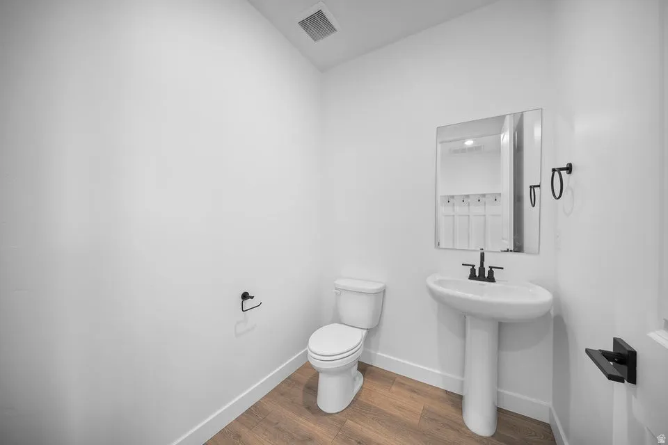 Pedestal sink with a wall-mounted rectangular mirror, black-finish faucet, and wood-finish flooring