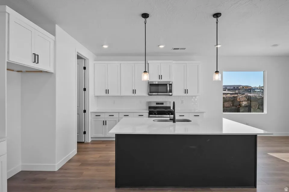 Kitchen featuring white shaker cabinetry, stainless steel appliances, a center island with pendant lighting, and wood-finish flooring