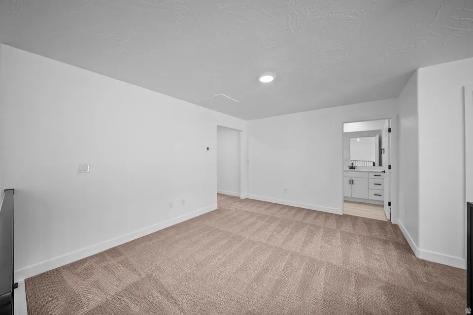 Neutral tone carpeting, white walls, recessed lighting, and a doorway to a bathroom with a white vanity