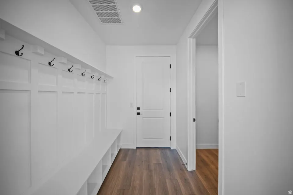 Built-in bench with integrated cubby storage, wall paneling with hooks, wood-finish flooring, recessed ceiling light, and interior door with black hardware