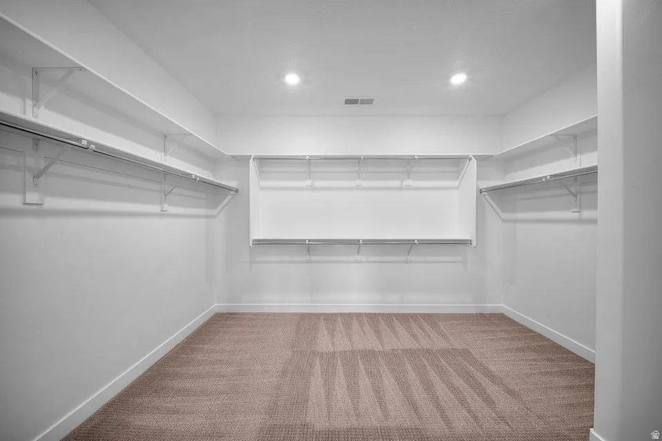 Spacious walk-in closet with extensive shelving and hanging rods, recessed lighting, and soft carpeting
