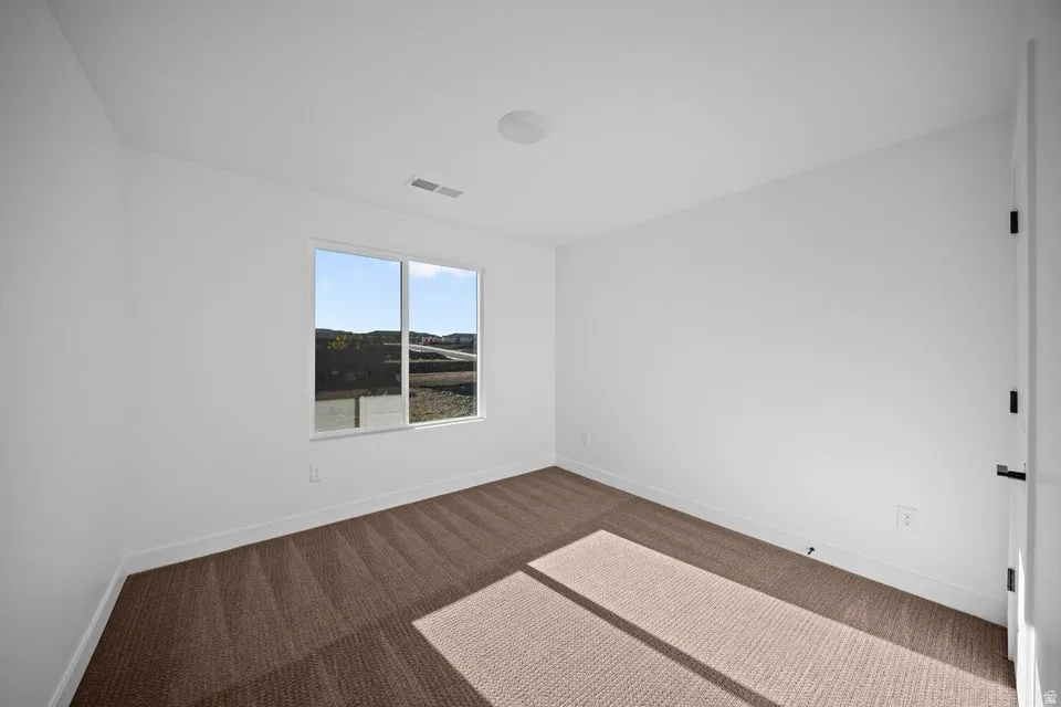 Neutral carpet flooring, white painted walls, large window, and recessed lighting