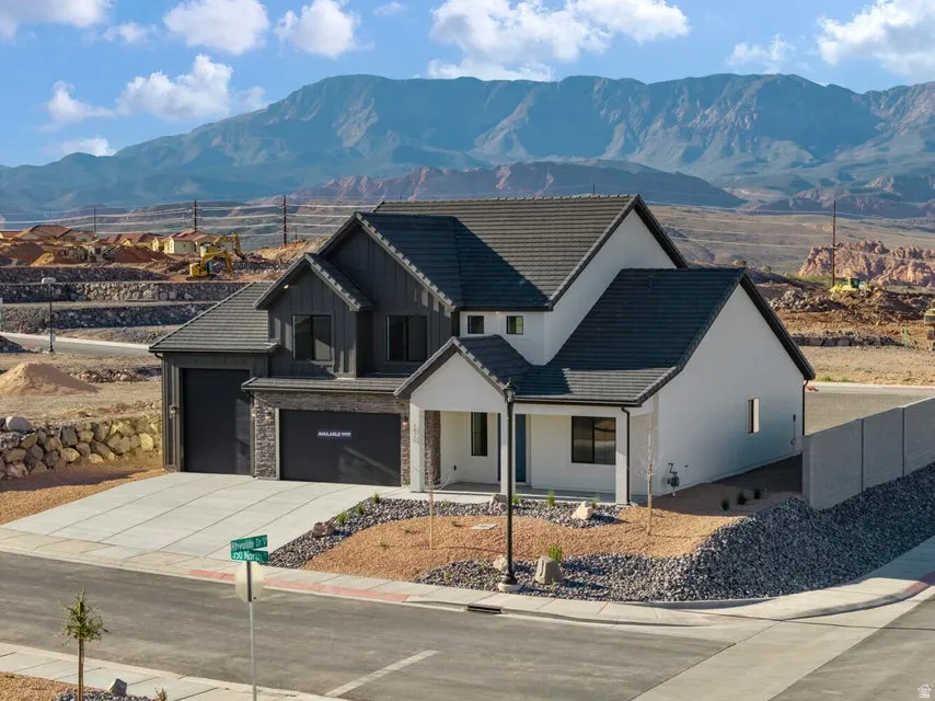 Modern exterior with contrasting dark and light siding, prominent mountain backdrop, attached two-car garage, covered entry, and xeriscaped front yard