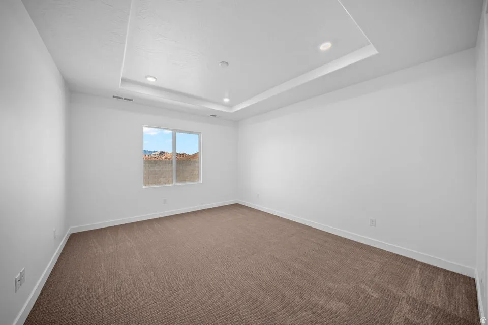 Recessed lighting, tray ceiling, neutral tone carpeting, white walls, and a large window
