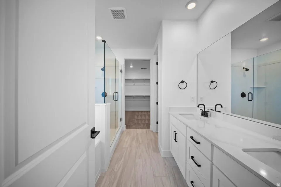 Dual vanity with white cabinetry and integrated sinks, glass-enclosed shower, wood-finish flooring, and recessed lighting