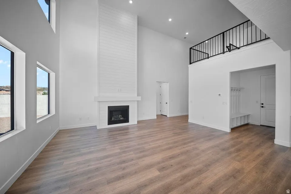 Two-story living area with high ceilings, wood-finish flooring, a built-in fireplace with white mantel, a built-in bench with coat hooks, and an open loft with a black railing