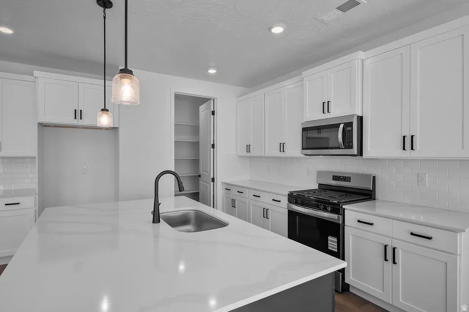 White shaker-style cabinetry, stainless steel appliances, a center island with an integrated sink, a matte black faucet, and pendant lighting