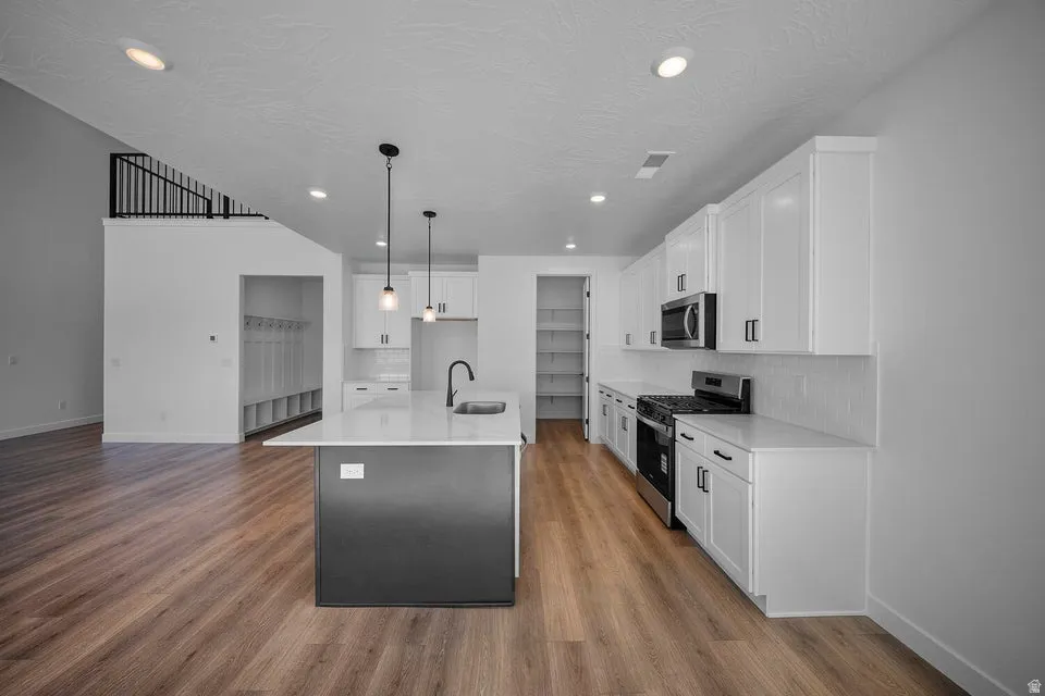 Modern kitchen featuring a central island with pendant lighting, stainless steel appliances, white cabinetry, and wood-finish flooring