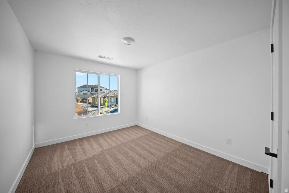 Clean white walls with a large window, recessed ceiling light, and brown patterned carpet