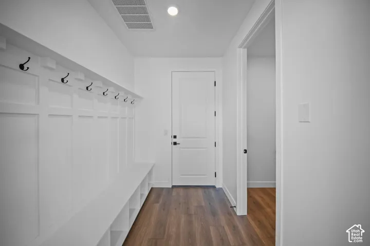 Built-in bench with integrated cubby storage, wall paneling with hooks, wood-finish flooring, recessed ceiling light, and interior door with black hardware