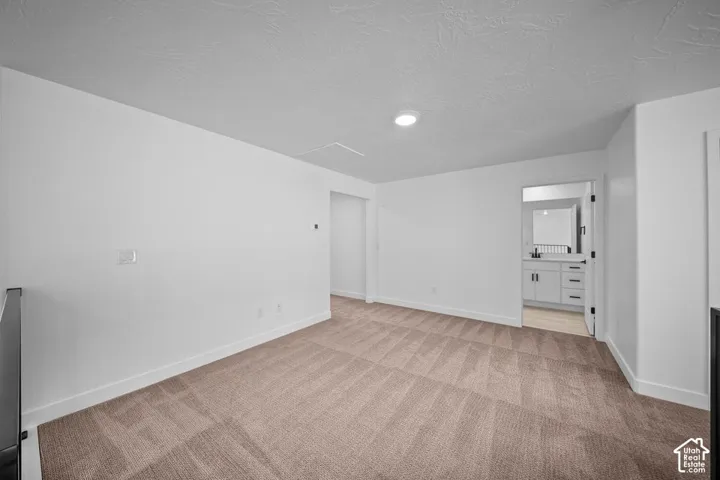 Neutral tone carpeting, white walls, recessed lighting, and a doorway to a bathroom with a white vanity