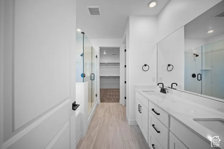 Dual vanity with white cabinetry and integrated sinks, glass-enclosed shower, wood-finish flooring, and recessed lighting