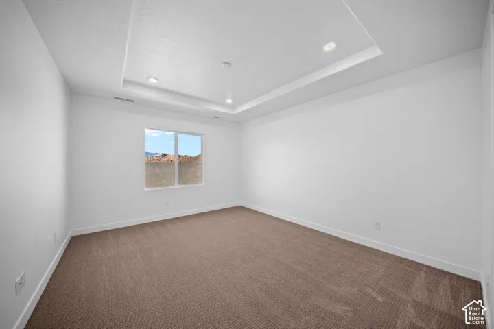 Recessed lighting, tray ceiling, neutral tone carpeting, white walls, and a large window