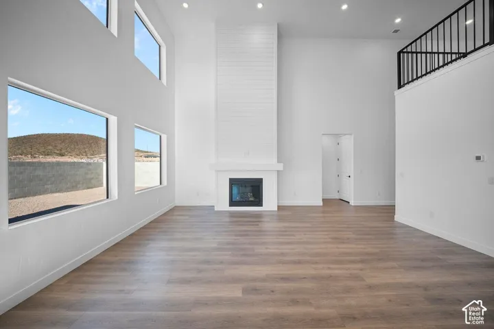 Spacious living area featuring high ceilings, wood-finish flooring, a contemporary fireplace with a shiplap surround, and multiple large windows