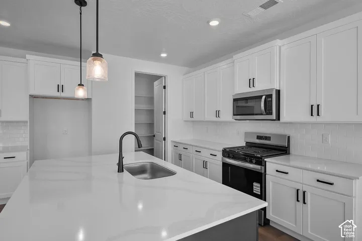 White shaker-style cabinetry, stainless steel appliances, a center island with an integrated sink, a matte black faucet, and pendant lighting