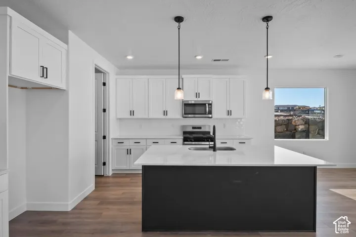 Kitchen featuring white shaker cabinetry, stainless steel appliances, a center island with pendant lighting, and wood-finish flooring