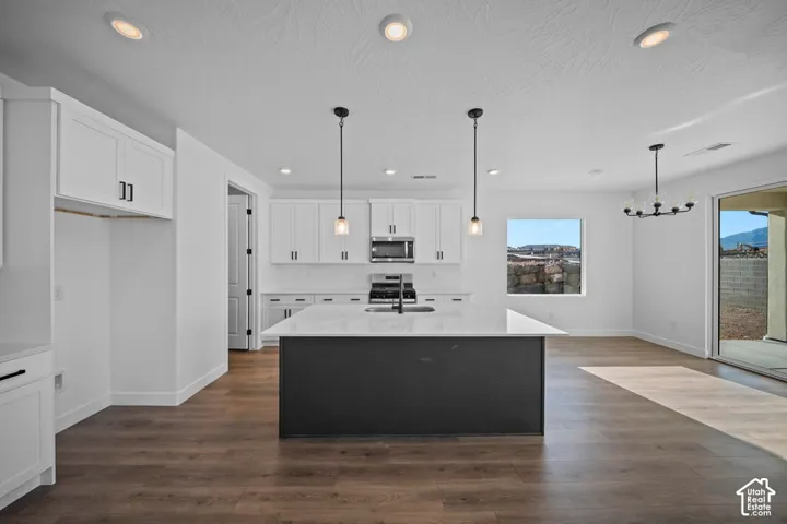 White cabinetry with dark hardware, a dark kitchen island, stainless steel appliances, wood-finish flooring, and a sliding glass door