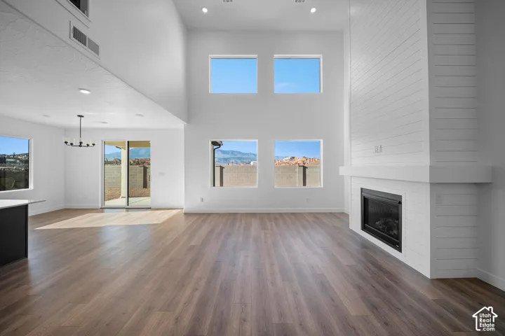 Spacious living area featuring high vaulted ceilings, large windows, wood-finish flooring, a contemporary fireplace with a shiplap surround, and a sliding glass door leading to an outdoor area