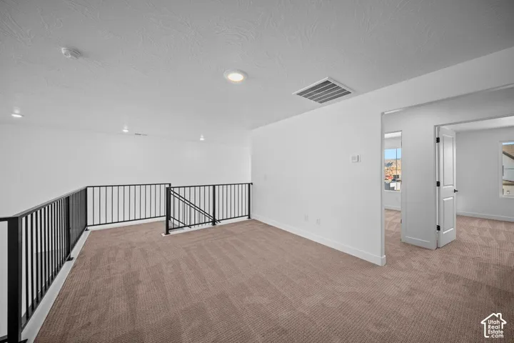 Carpeted loft area featuring black metal railing, recessed lighting, and white interior walls