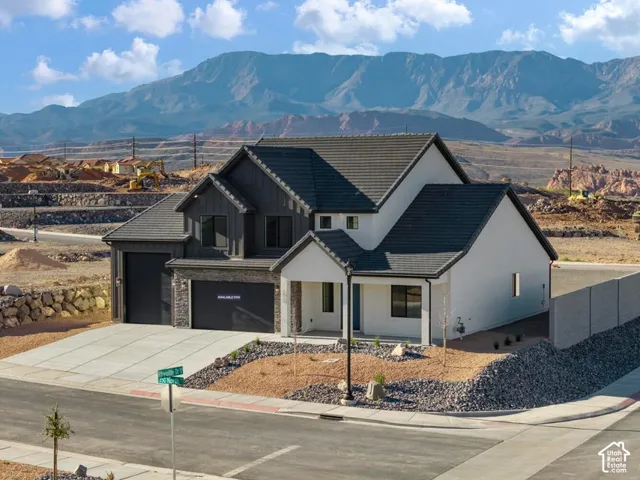 Modern exterior with contrasting dark and light siding, prominent mountain backdrop, attached two-car garage, covered entry, and xeriscaped front yard