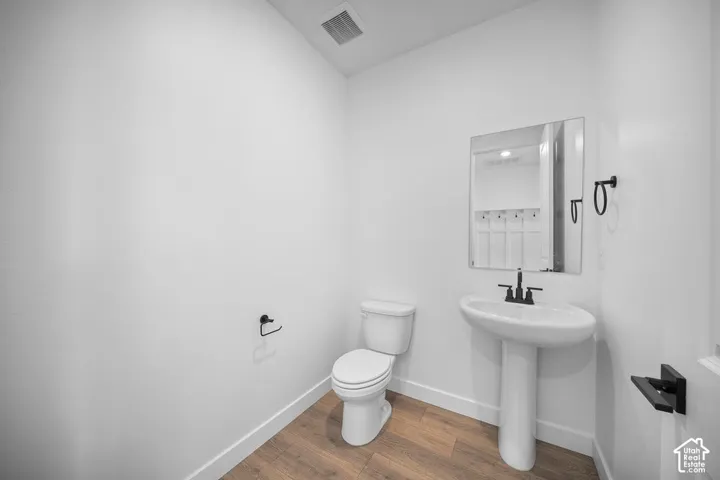 Pedestal sink with a wall-mounted rectangular mirror, black-finish faucet, and wood-finish flooring