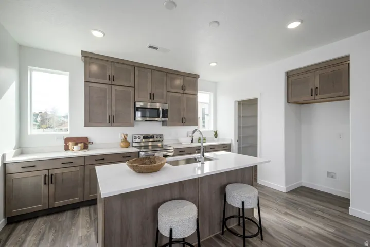 Kitchen featuring wood-finish cabinetry, stainless steel appliances, a center island with sink, white countertops, and wood-finish flooring