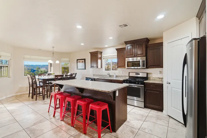 Kitchen featuring wood cabinetry, stainless steel appliances, a center island with a light-toned countertop, and light-toned tile flooring