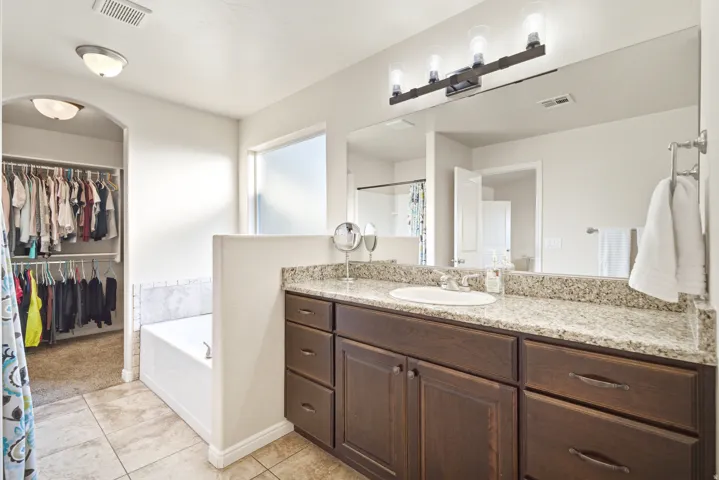 Granite-look countertop, wood-finish cabinetry, built-in bathtub, tile flooring, and dedicated closet space