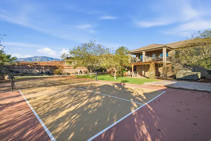 Sport court with painted lines, stucco exterior, upper-level balcony, lower-level patio, and surrounding landscaping