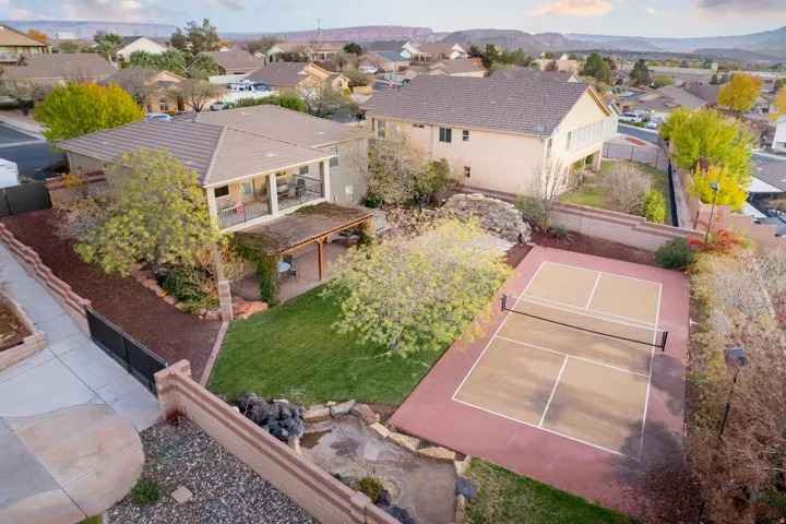 Expansive backyard featuring a dedicated sports court, a manicured lawn, a covered patio, a second-story balcony, and mature landscaping