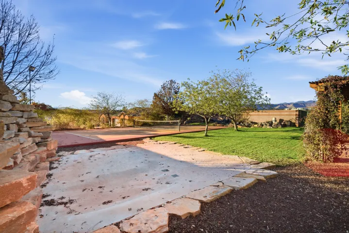 Red clay tennis court, flagstone patio, lush lawn, stone retaining wall, and mature landscaping