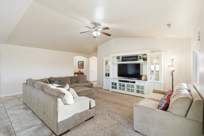 Spacious open-concept family room featuring vaulted ceilings, a ceiling fan with integrated lighting, and neutral carpeting throughout