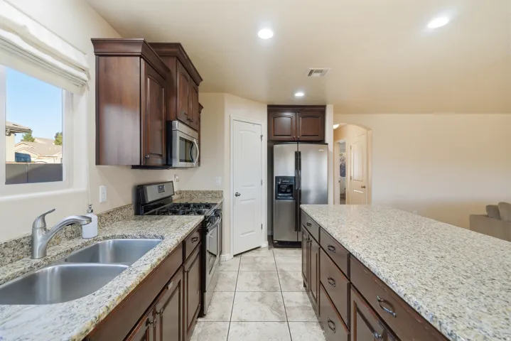 Kitchen featuring a dual basin stainless steel sink, granite countertops, stainless steel appliances, dark wood cabinetry, and recessed lighting