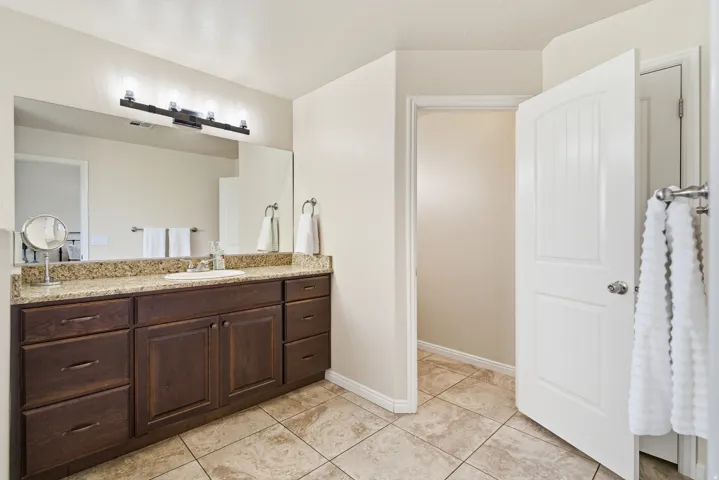 Warm-toned tile flooring, an expansive vanity mirror, and a dark wood-finish vanity with a light-toned countertop
