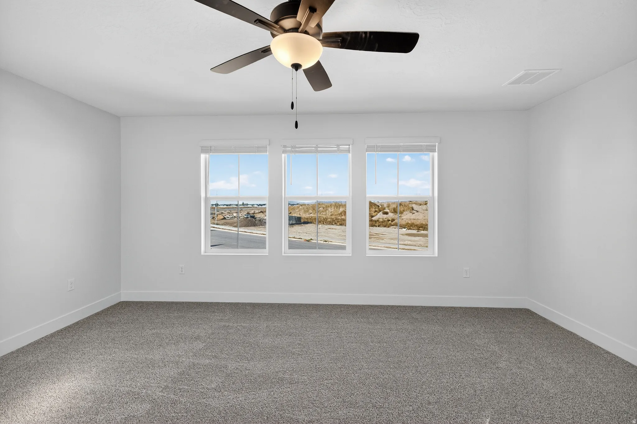 Spacious room featuring three large windows, a ceiling fan with integrated lighting, and neutral carpeting