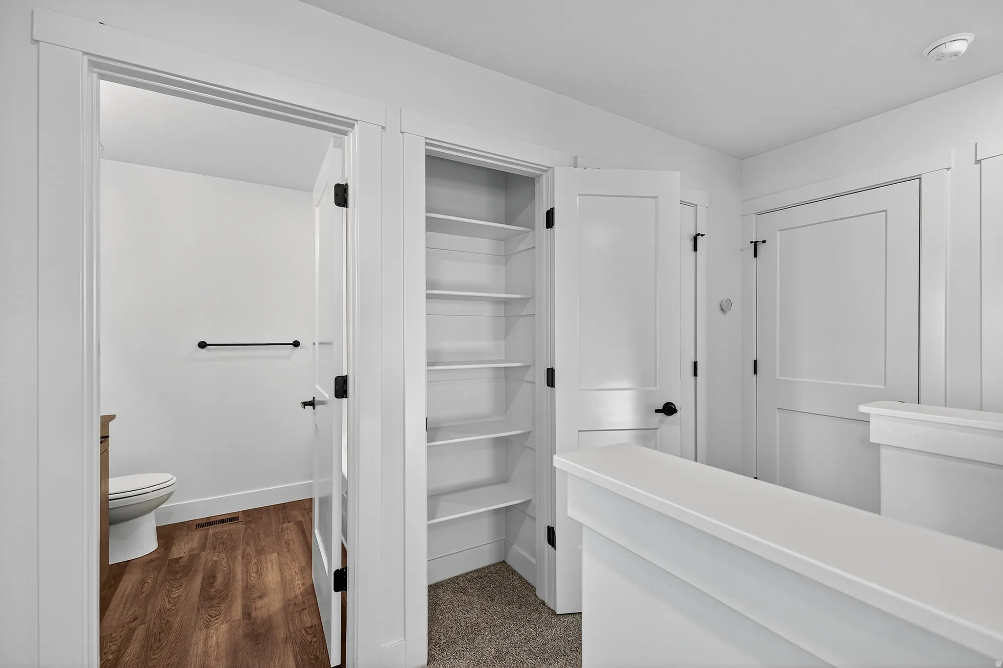 Recessed shelving, wood-finish flooring, white paneled doors, and black door hardware