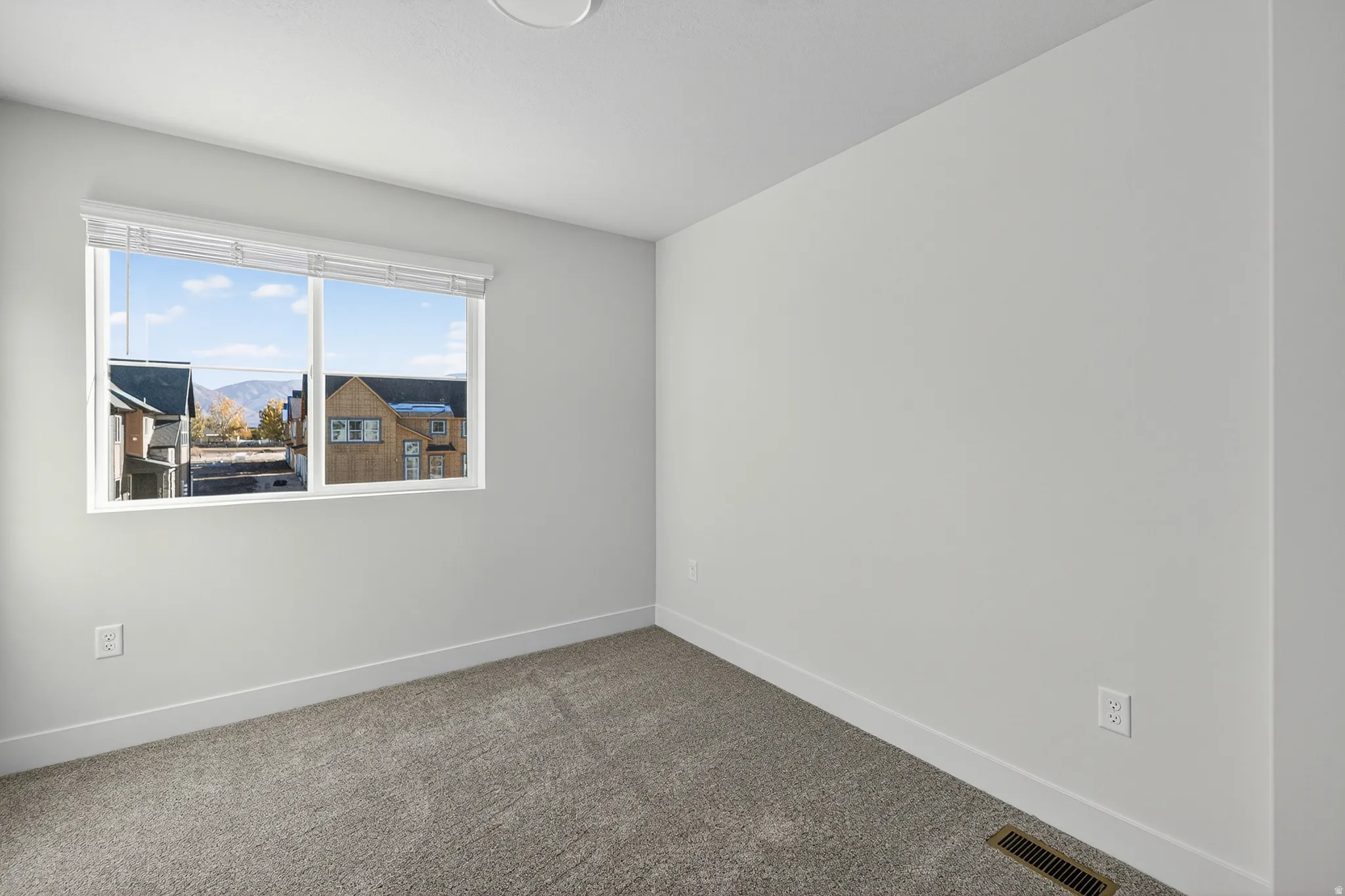 Neutral wall paint, plush carpeting, white window blinds, and a white-framed window