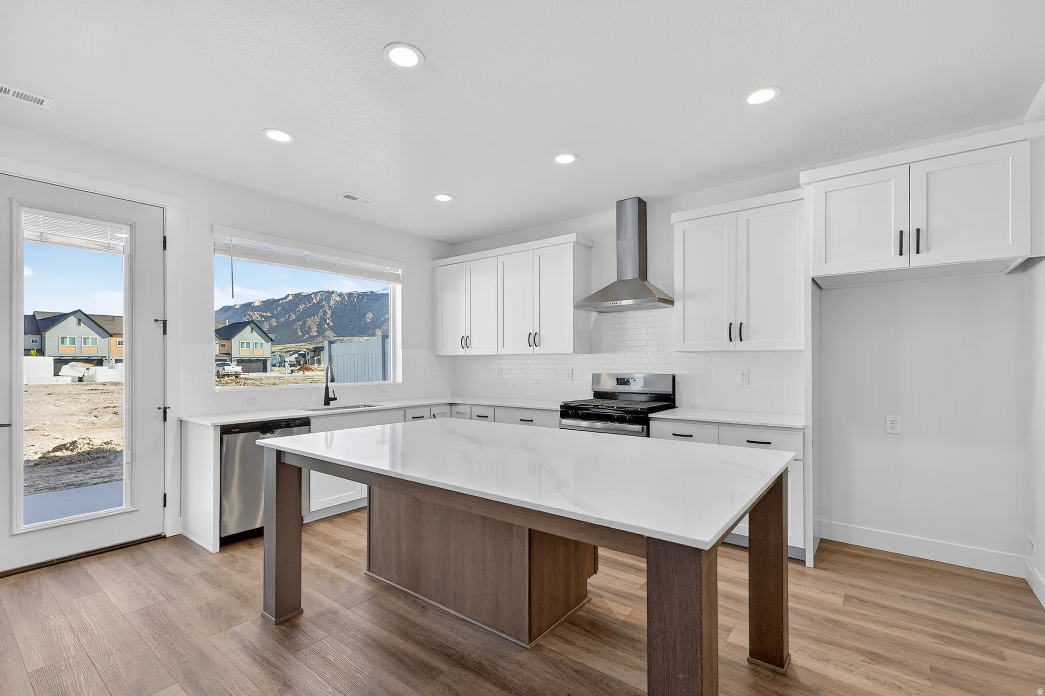 Modern kitchen featuring white cabinetry, stainless steel appliances, a white tile backsplash, and a large center island with a light-colored countertop