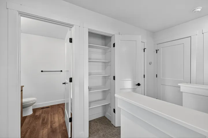 Recessed shelving, wood-finish flooring, white paneled doors, and black door hardware