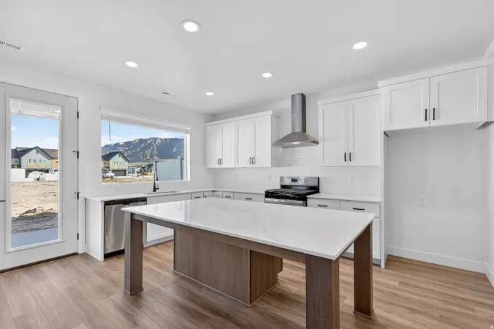 Modern kitchen featuring white cabinetry, stainless steel appliances, a white tile backsplash, and a large center island with a light-colored countertop