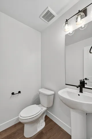 Pedestal sink with a matte black faucet, wall-mounted mirror, and wood-finish flooring