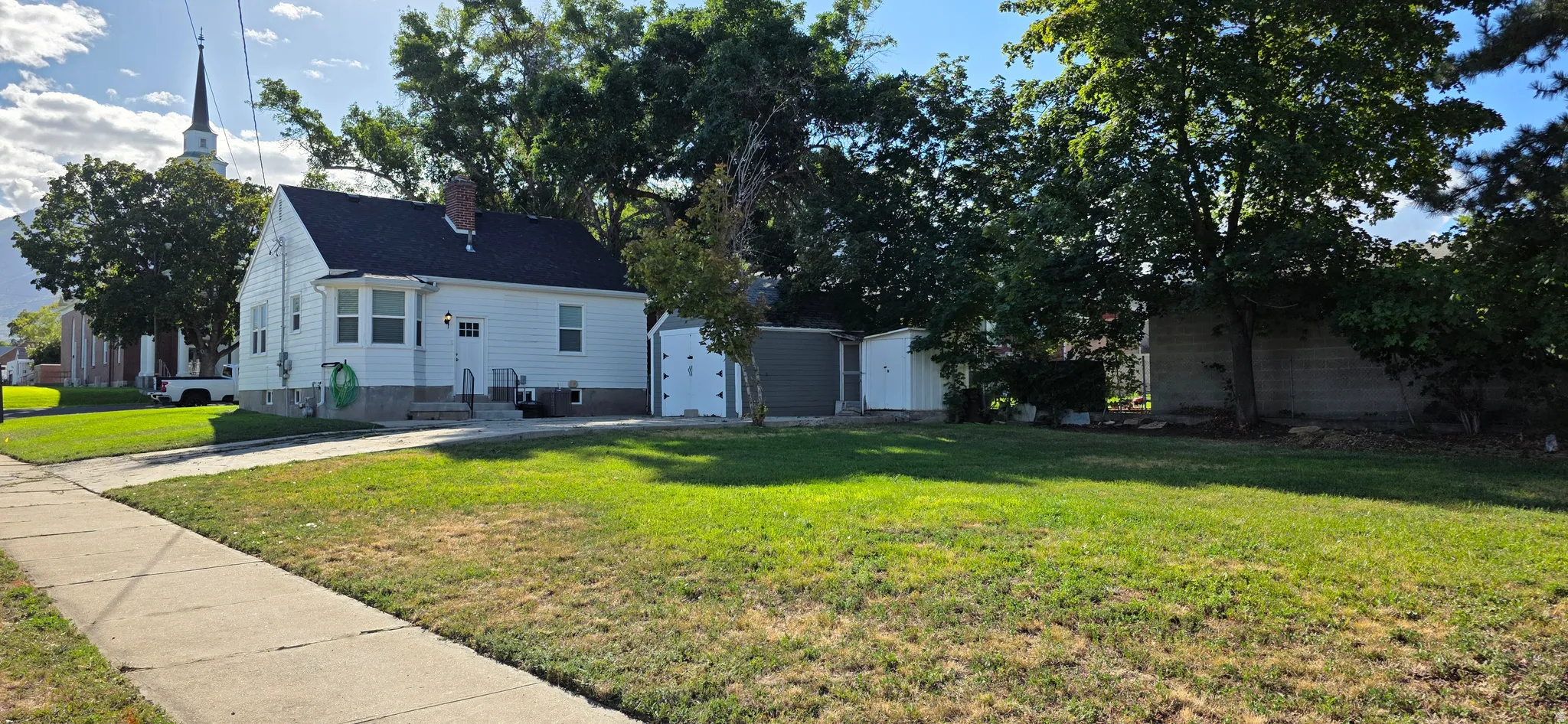 White siding exterior with a dark shingle roof, chimney, and a concrete driveway