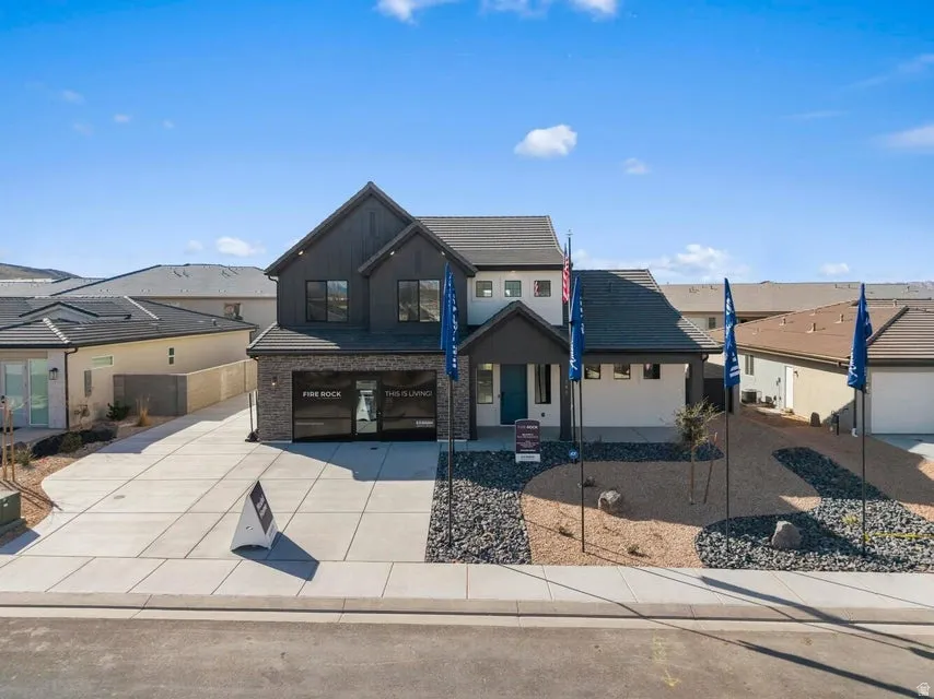 Contemporary exterior featuring board and batten siding, brick accents, a two-car garage with a glass panel door, an extended concrete driveway, and desert-inspired landscaping
