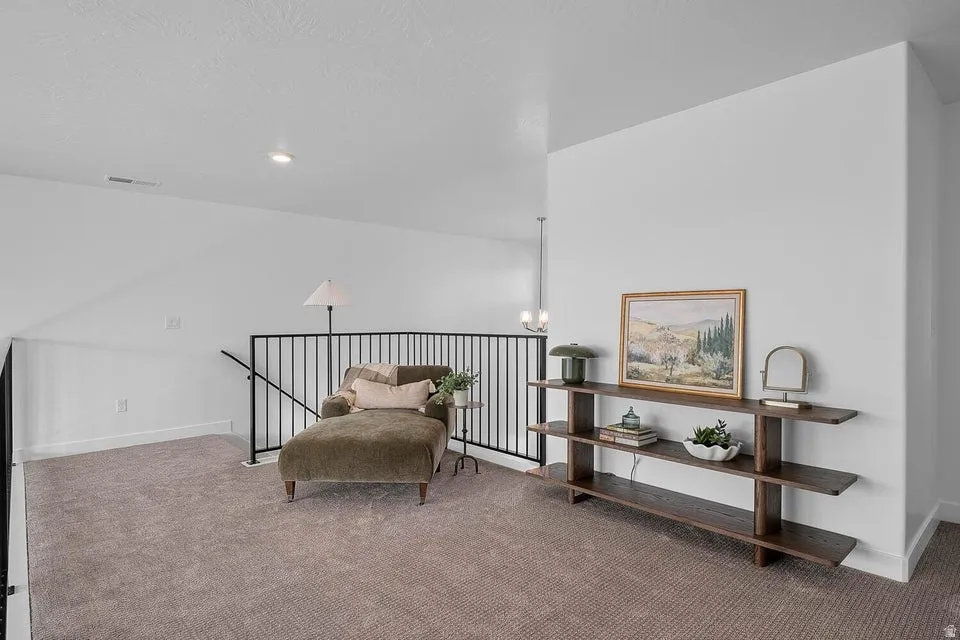 Carpeted loft area featuring a dark metal railing, recessed lighting, and a contemporary wall console