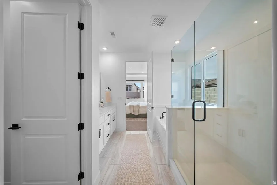 Bathroom featuring a glass-enclosed shower, built-in soaking tub, dual vanity with white cabinetry, and wood-finish flooring