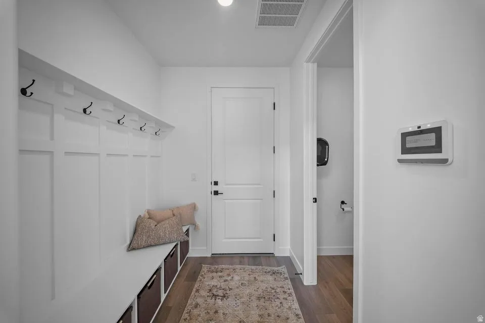 Board and batten wall with integrated bench seating, black coat hooks, wood-finish flooring, and a solid panel interior door with matte black hardware