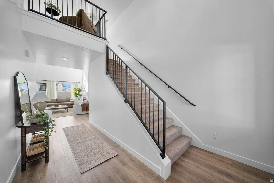 Wood-finish flooring, carpeted staircase with dark metal railing, and an upper-level balcony with a matching dark metal railing