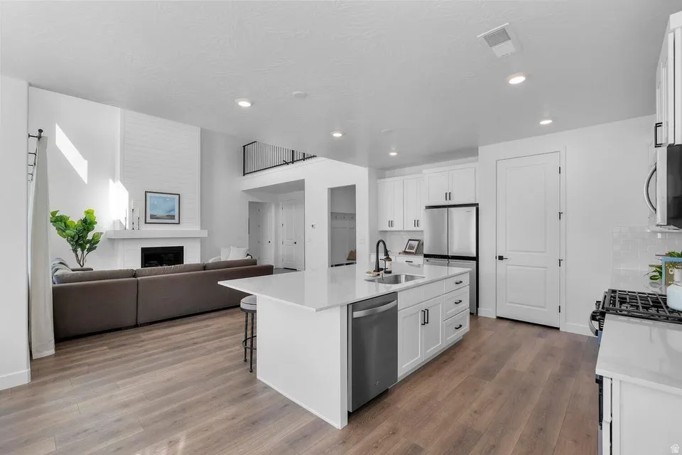 Open-concept living space with wood-finish flooring, a white kitchen island, and stainless steel appliances