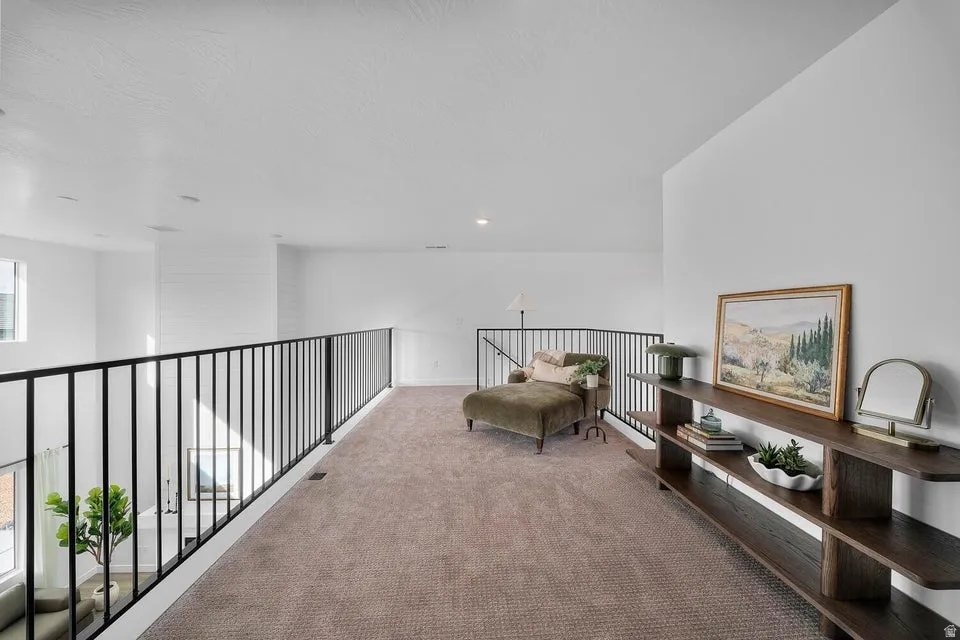 Spacious loft area featuring carpeting, white walls, black metal railing, and a built-in dark wood shelving unit