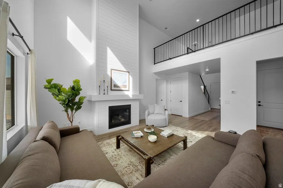 Two-story living area featuring a fireplace with a shiplap accent wall, high ceilings, and wood-finish flooring